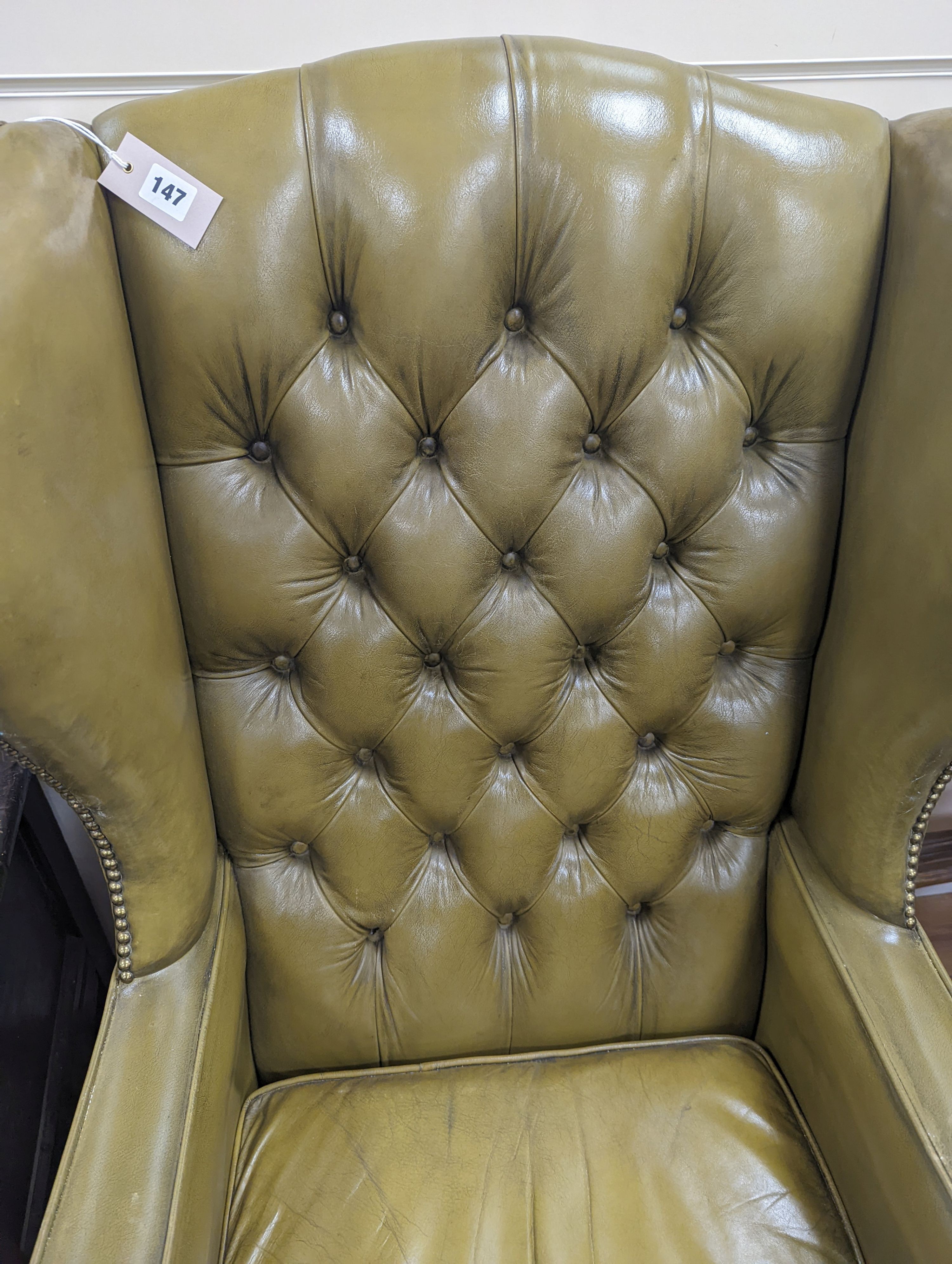 A George III style wing armchair upholstered in studded buttoned green leather, width 79cm, depth 76cm, height 116cm